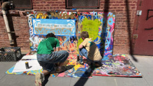 Two people painting on a wall outside