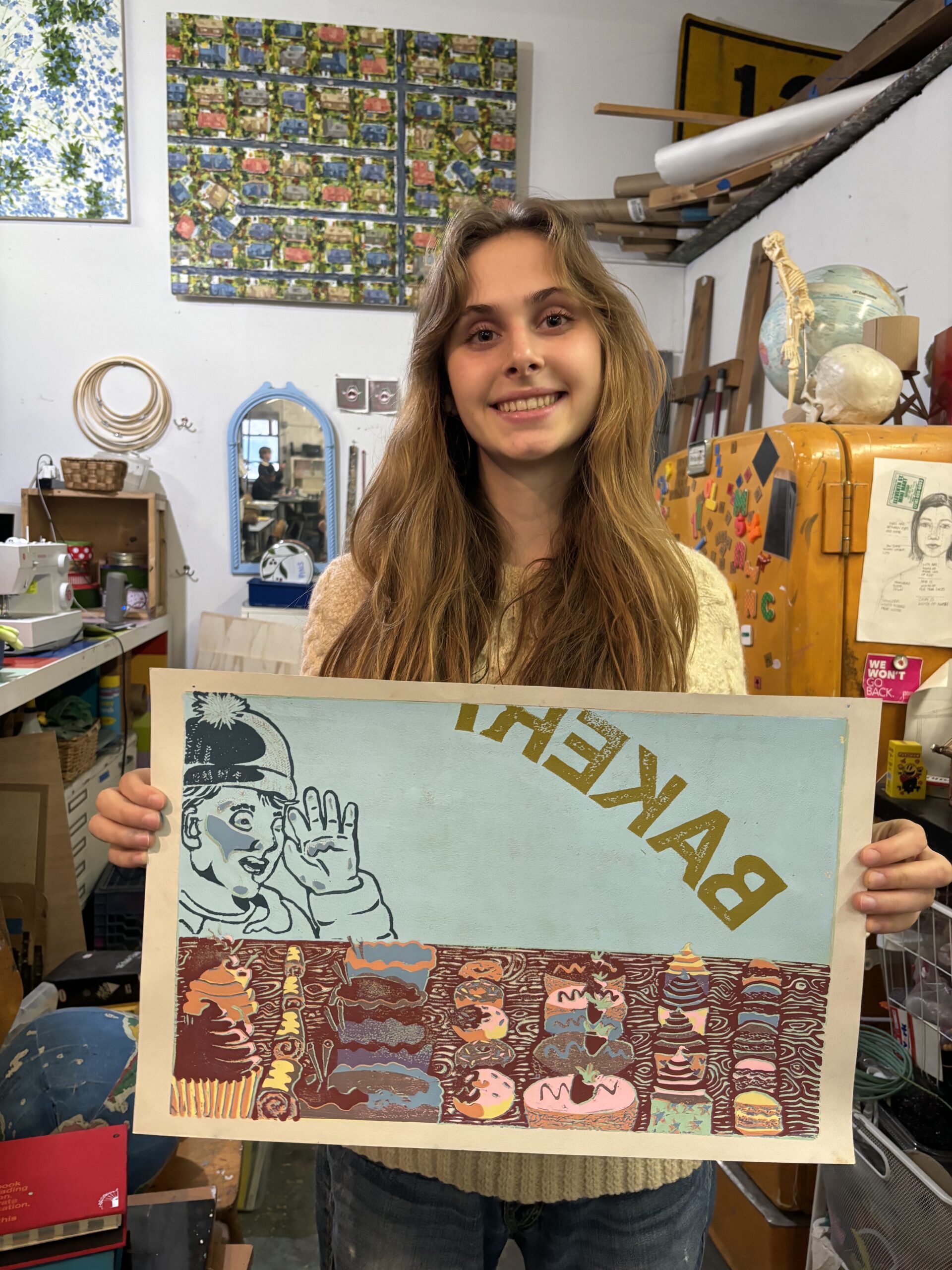 A girl holding up a poster in front of many other paintings.