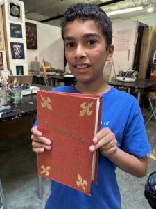 A boy holding up an old book in front of him.