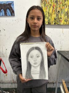 A girl holding up a drawing of herself.