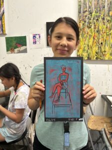 A girl holding up an art project in front of her face.
