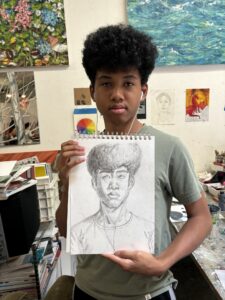 A young man holding up a drawing of himself.