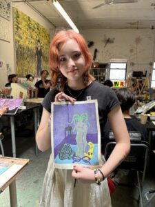 A girl holding up an art project in front of other people.