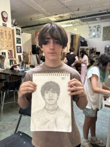 A boy holding up a drawing of himself.