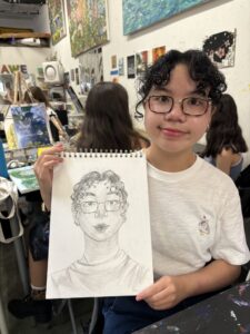 A girl holding up a drawing of herself.