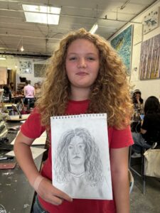 A girl holding up a drawing of herself.