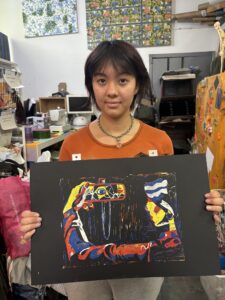 A girl holding up an abstract painting in front of other people.