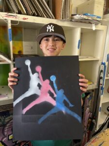 A boy holding up a painting of three people in the air.