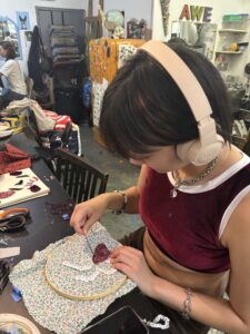 A woman wearing headphones is sewing on a piece of fabric.