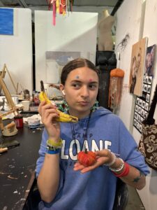A girl holding a banana and tomato in her hand.