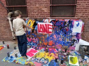 A boy is painting graffiti on the side of a building.