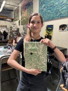 A girl holding up a book with green and white designs.