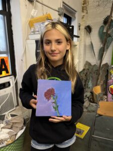 A girl holding up a painting of a rose.