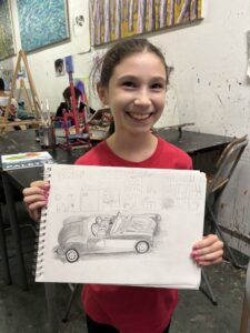 A girl holding up a drawing of a car.