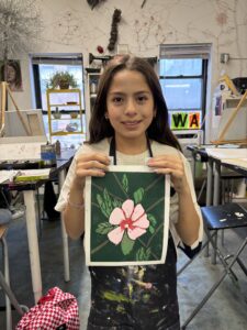 A girl holding up a painting of a flower.