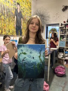 A girl holding up an underwater painting in front of other girls.
