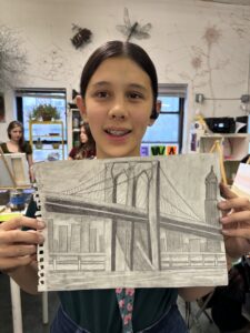 A girl holding up a drawing of the brooklyn bridge.