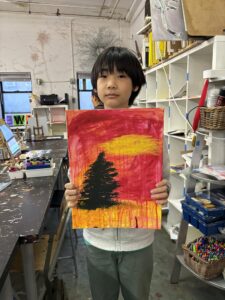 A young person holding up an orange and yellow painting.