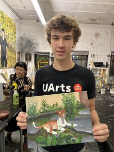 A man holding up an animal painting in front of another person.
