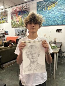 A young man holding up a drawing of himself.