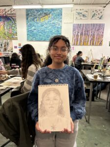 A girl holding up a drawing of herself.