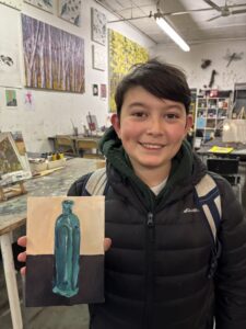 A young boy holding up a painting of a bottle.