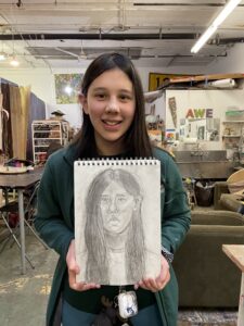 A girl holding up a drawing of herself.