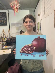 A woman holding up a painting of an open pomegranate.