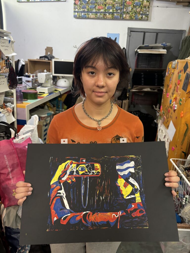 A girl holding up an abstract painting in front of other paintings.