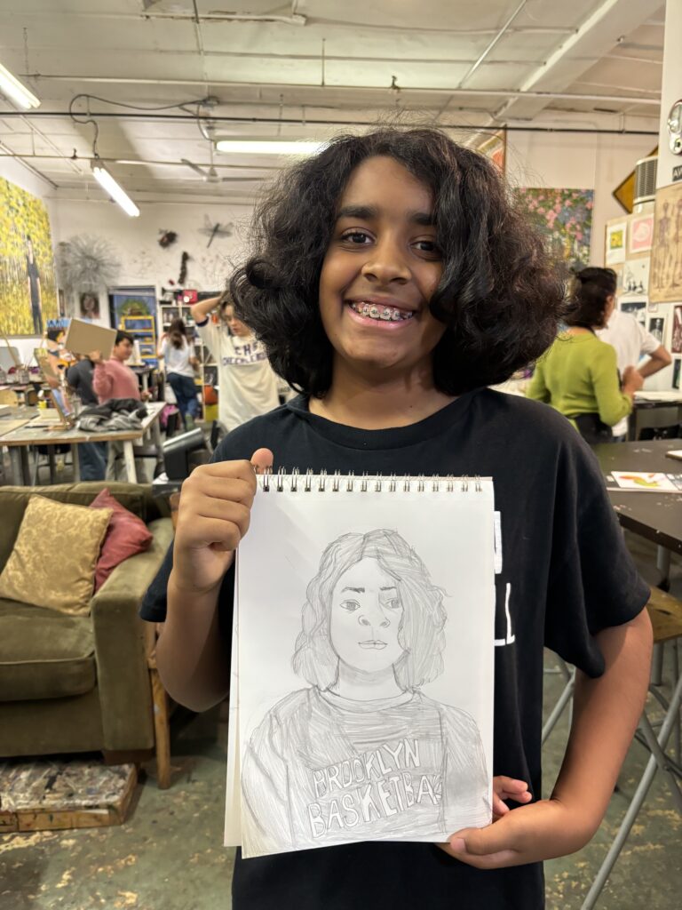 A young person holding up a drawing of a woman.