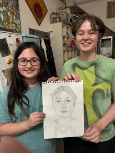 Two girls showing a pencil portrait.
