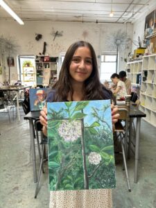 Girl holding painting of flowering plant.
