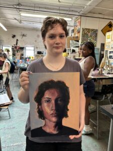 Student proudly displays painted portrait.