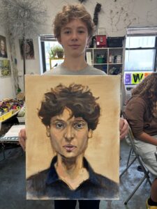 Teenager proudly displays his portrait painting.