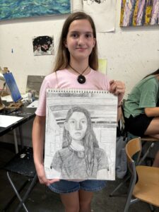 Girl proudly displays her pencil self-portrait.