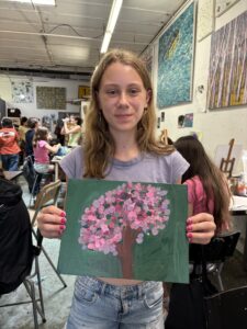 Girl holding painting of pink tree.