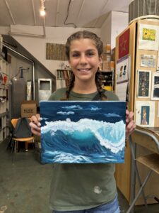 Girl proudly displays ocean wave painting.