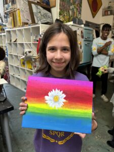 Girl holding rainbow daisy painting.