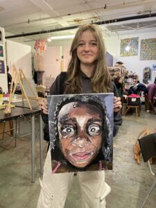 Student proudly displays portrait painting.