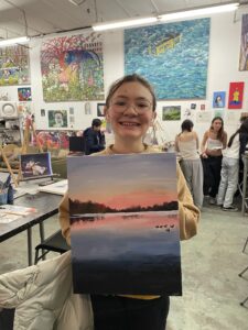 Girl proudly displays her sunset painting.