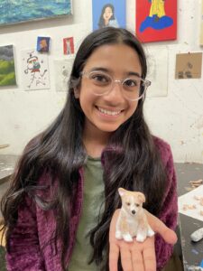 Smiling girl holding clay corgi sculpture.