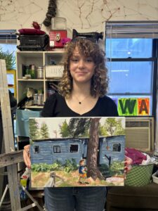 Woman holding painting of blue house.