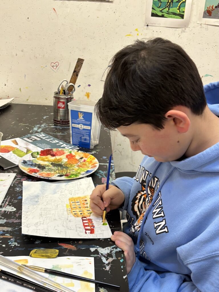 A boy painting watercolors with focus at a table.