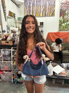 Smiling woman holding a handmade denim bag with pink accents indoors.