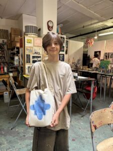 Young person holding a tote bag with blue paint design in an art studio.