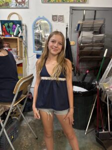A smiling young woman in a black tank top and shorts poses indoors.