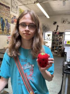 A young person holding a red craft heart in an art studio.