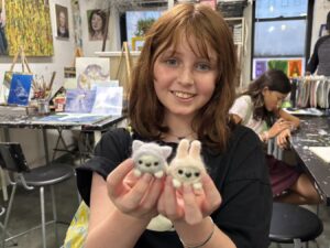 A young woman holding two cute crocheted animal toys with a smile.