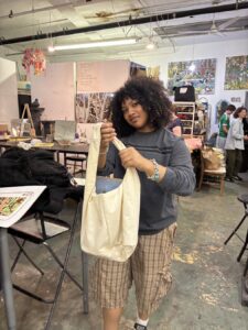 Person smiling while holding a beige tote bag in an art studio.