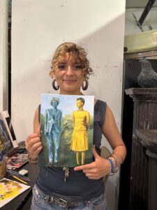 Woman holding a surrealist painting of two abstract figures in blue and yellow dresses.